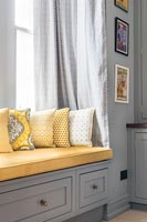 Grey built-in wooden window seat with yellow cushions