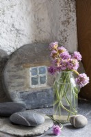 Vase of wild flowers (Sea Pinks) and decorative pebbles on shelf